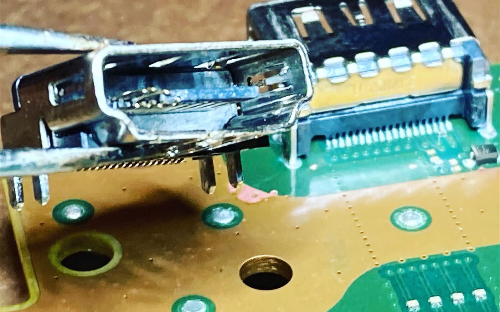 Damaged PS5 HDMI port held in tweezers beside the new replacement port installed on the console board